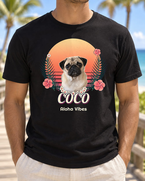 Black personalized Hawaiian dog T-shirt on a beach boardwalk, showing Coco the pug with a flower lei, sunset, palms, hibiscus and Aloha Vibes lettering.