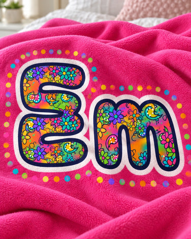 Close-up of the bubble letter print on a hot pink fleece name blanket: paisley and flower pattern, white outline and coloured dots