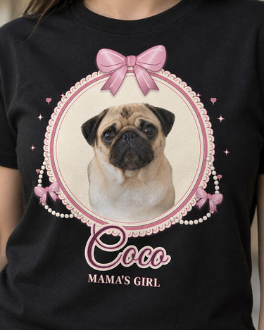 Close-up of a black coquette dog shirt showing the cream oval cameo, scalloped lace, pink satin-style bows, round pearl strands and Coco in outlined script.