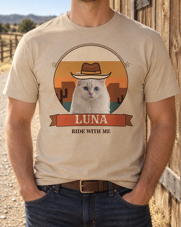 Sand western pet photo shirt on an adult by a timber barn, with a white cat in a cowboy hat, a warm desert sunset, cactus silhouettes and the name LUNA.