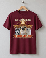 Maroon Rodeo Star pet photo tee on a wooden hanger against a plank wall, showing three cowboy-hatted pets above a rust-red banner reading THE POSSE.