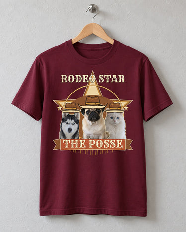 Maroon Rodeo Star pet photo tee on a wooden hanger against a plank wall, showing three cowboy-hatted pets above a rust-red banner reading THE POSSE.
