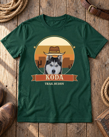 Forest green Desert Sunset pet photo tee laid on barn wood beside rope, a plain leather belt and cowboy boots, with a cowboy-hatted husky and the name KODA.