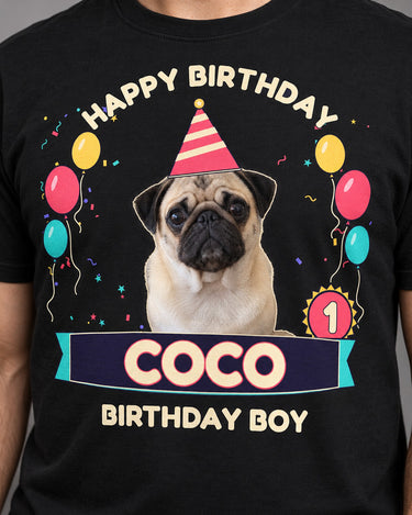 Close-up of the black pet birthday tee print showing the outlined pug, striped hat, cream Coco lettering and pink age 1 rosette.