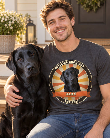 Smiling man with his black Labrador sitting on porch steps, wearing a charcoal grey pet vintage badge t-shirt that shows the same dog in a sunburst badge