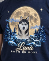 Close-up of the full moon print on a navy t-shirt: a husky on a snow-capped rock between pine trees with glowing script lettering
