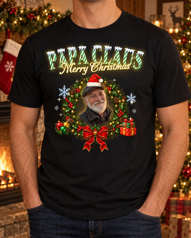Man wearing a black custom face Christmas t-shirt with a grandfather's face in a Santa hat inside a wreath and the name Papa Claus in mint green candy-cane letters