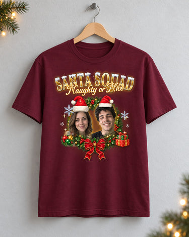 Maroon custom face Christmas t-shirt on a wooden hanger with two faces in Santa hats inside a holly wreath and gold lettering