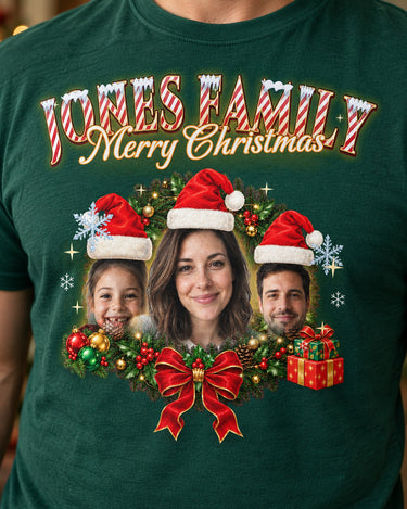 Close-up of the full-color print on a forest green face Christmas t-shirt: three faces in Santa hats in a holly wreath with a red bow