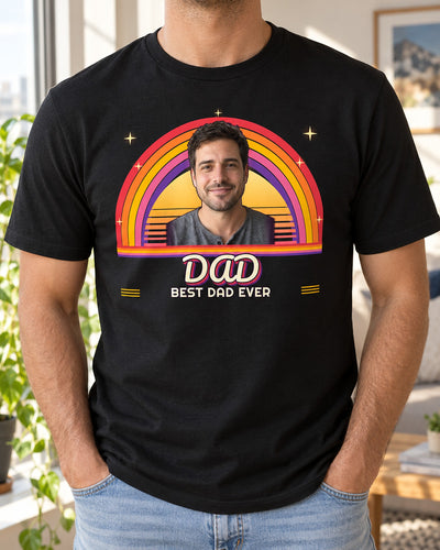 Black custom retro photo shirt worn in a bright apartment, with a portrait above a striped sunset, red-to-purple rainbow arcs and DAD in groovy script.