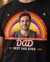 Close-up of the black DAD photo tee showing portrait edges, a cream-to-coral striped sun, five sunset rainbow arcs and layered groovy script lettering.