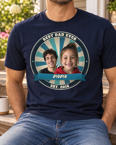 Man sitting on porch steps wearing a navy Dad Est. photo badge t-shirt with two kids' faces, ocean badge colors and the name Papa