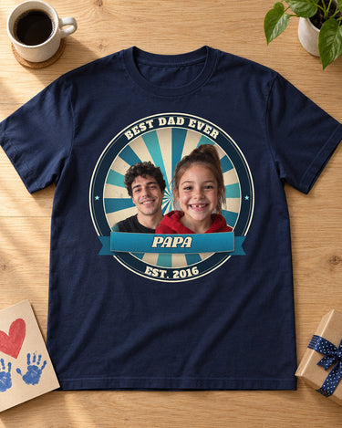 Navy Dad Est. photo badge t-shirt laid flat on an oak table with a Father's Day card, coffee mug and gift, two kids' faces in an ocean badge with the name Papa