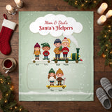 Mom and Dad's Santa's Helpers personalized blanket with kids names laid flat on a wooden floor with Christmas stocking and candles