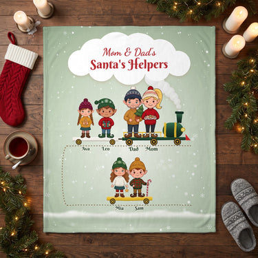 Mom and Dad's Santa's Helpers personalized blanket with kids names laid flat on a wooden floor with Christmas stocking and candles
