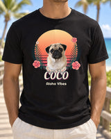 Black personalized Hawaiian dog T-shirt on a beach boardwalk, showing Coco the pug with a flower lei, sunset, palms, hibiscus and Aloha Vibes lettering.