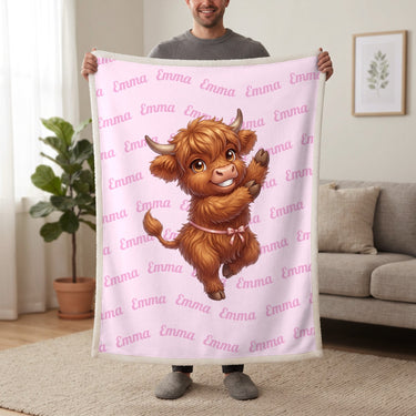 Personalized Highland cow dancing blanket in cotton pink held up in a living room, with the name Emma repeated in soft waves