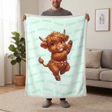 Personalized Highland cow dancing blanket in mint held up in a living room, with the name Emma repeated in soft waves
