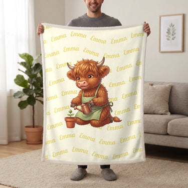 Personalized Highland cow gardener blanket in lemon cream held up in a living room, with the name Emma repeated in soft waves