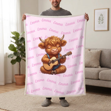 Personalized Highland cow guitar blanket in cotton pink held up in a living room, with the name Emma repeated in soft waves
