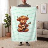 Personalized Highland cow guitar blanket in mint held up in a living room, with the name Emma repeated in soft waves