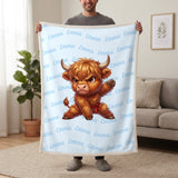 Personalized Highland cow karate blanket in baby blue held up in a living room, with the name Emma repeated in soft waves