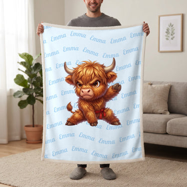 Personalized Highland cow karate blanket in baby blue held up in a living room, with the name Emma repeated in soft waves