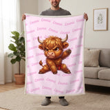 Personalized Highland cow karate blanket in cotton pink held up in a living room, with the name Emma repeated in soft waves