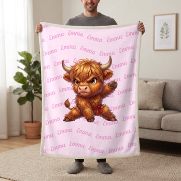 Personalized Highland cow karate blanket in cotton pink held up in a living room, with the name Emma repeated in soft waves
