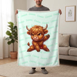 Personalized Highland cow karate blanket in mint held up in a living room, with the name Emma repeated in soft waves