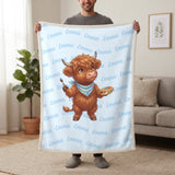 Personalized Highland cow painter blanket in baby blue held up in a living room, with the name Emma repeated in soft waves