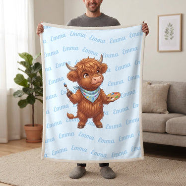Personalized Highland cow painter blanket in baby blue held up in a living room, with the name Emma repeated in soft waves