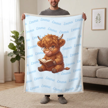 Personalized Highland cow reading blanket in baby blue held up in a living room, with the name Emma repeated in soft waves