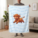 Personalized Highland cow running blanket in baby blue held up in a living room, with the name Emma repeated in soft waves