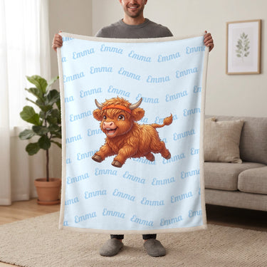 Personalized Highland cow running blanket in baby blue held up in a living room, with the name Emma repeated in soft waves