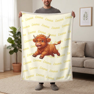 Personalized Highland cow running blanket in lemon cream held up in a living room, with the name Emma repeated in soft waves