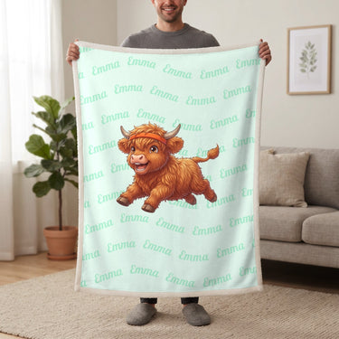 Personalized Highland cow running blanket in mint held up in a living room, with the name Emma repeated in soft waves