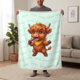Personalized Highland cow singer blanket in mint held up in a living room, with the name Emma repeated in soft waves