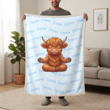 Personalized Highland cow yoga blanket in baby blue held up in a living room, with the name Emma repeated in soft waves
