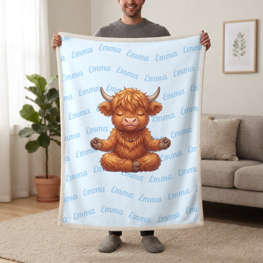 Personalized Highland cow yoga blanket in baby blue held up in a living room, with the name Emma repeated in soft waves