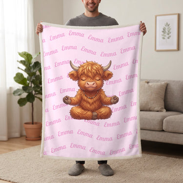 Personalized Highland cow yoga blanket in cotton pink held up in a living room, with the name Emma repeated in soft waves
