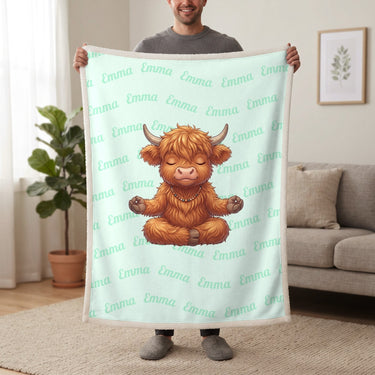 Personalized Highland cow yoga blanket in mint held up in a living room, with the name Emma repeated in soft waves