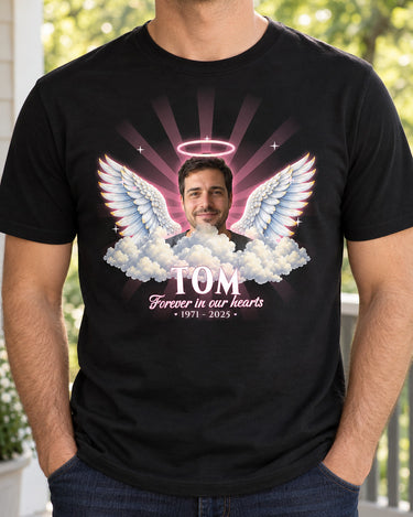 Man wearing a black in loving memory angel wings t-shirt with a man's photo, a rose-colored halo and the name Tom