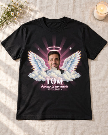 Black in loving memory angel wings t-shirt laid flat on a linen cloth with white wildflowers and a lit candle