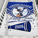 Royal blue cheerleader keepsake blanket with custom photo, name and graduation year folded over the side of a wooden crib