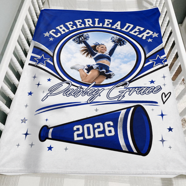 Royal blue cheerleader keepsake blanket with custom photo, name and graduation year folded over the side of a wooden crib