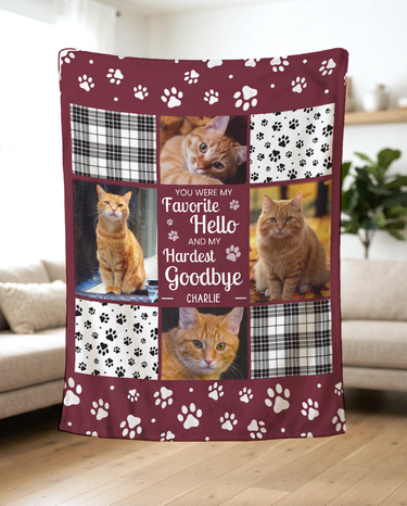 Favorite Hello Hardest Goodbye pet memorial blanket held up in a bright living room to show the soft fleece, four photos and white paw prints