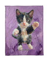Flat lay of a personalised kitten portrait blanket with an oil painted black and white kitten raising a paw on lavender brushstrokes and the name Luna