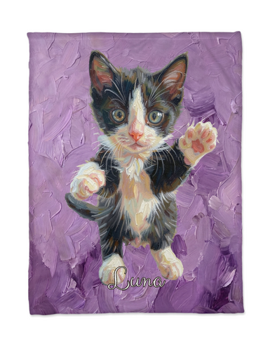 Flat lay of a personalised kitten portrait blanket with an oil painted black and white kitten raising a paw on lavender brushstrokes and the name Luna