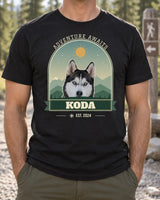 Black custom national-park-style pet photo shirt at a pine trailhead, showing Koda the husky in a green mountain arch with Adventure Awaits above.